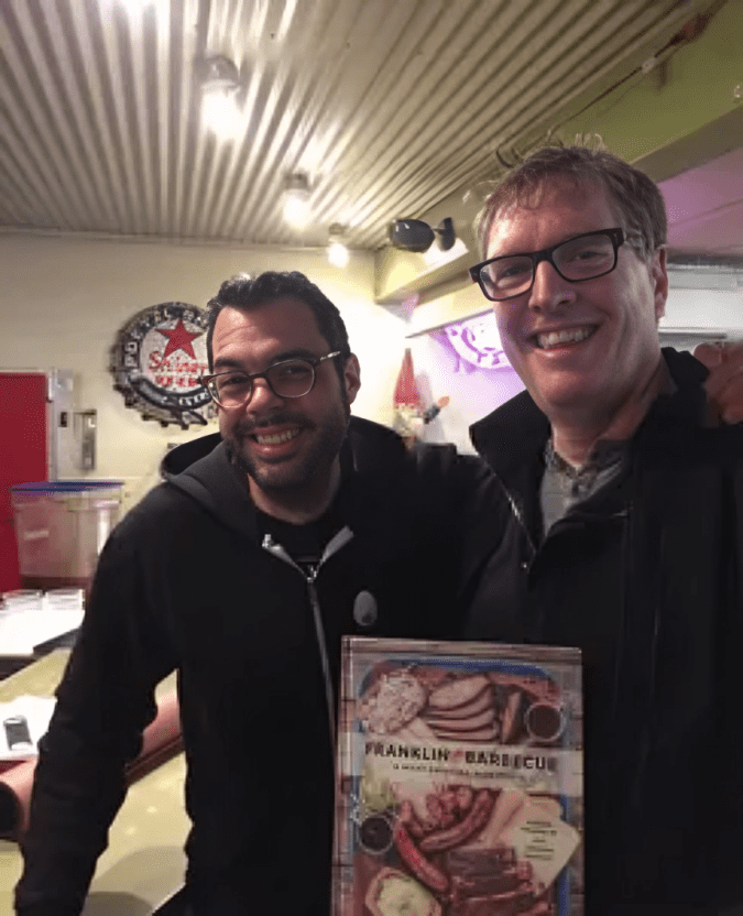 Two men smile while holding a book.