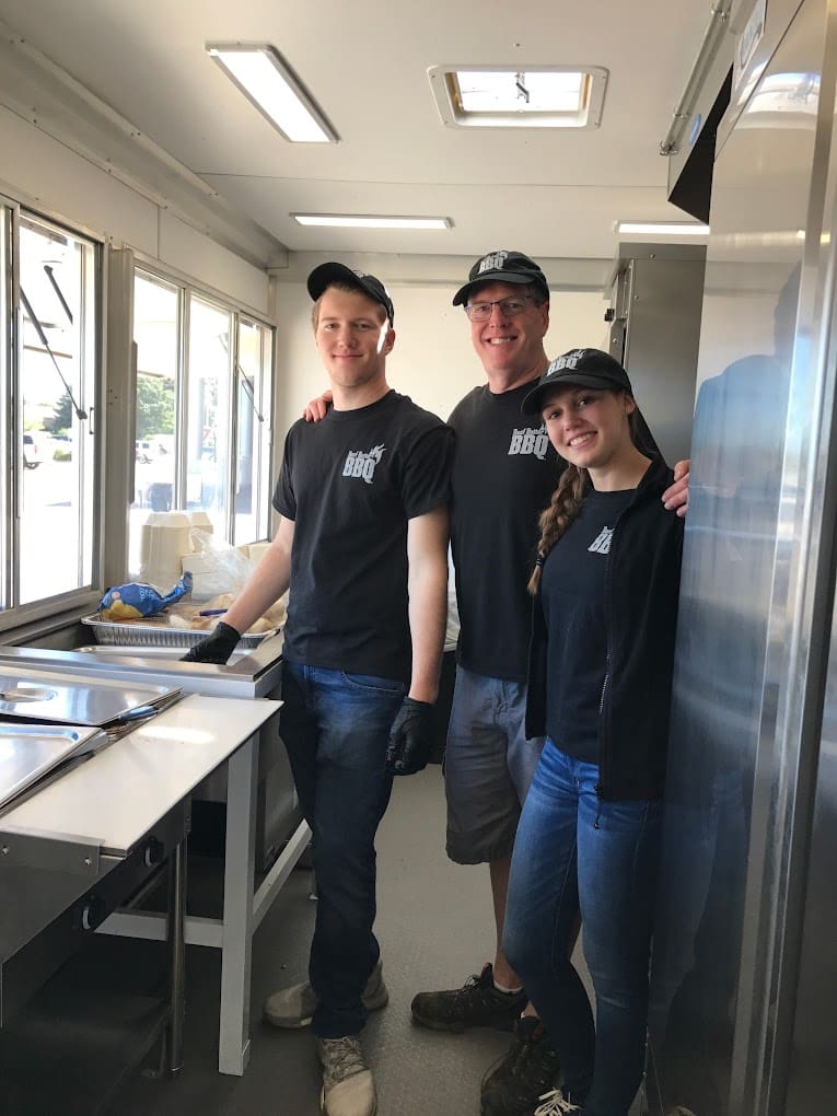 Three people standing in a kitchen with one of them smiling.