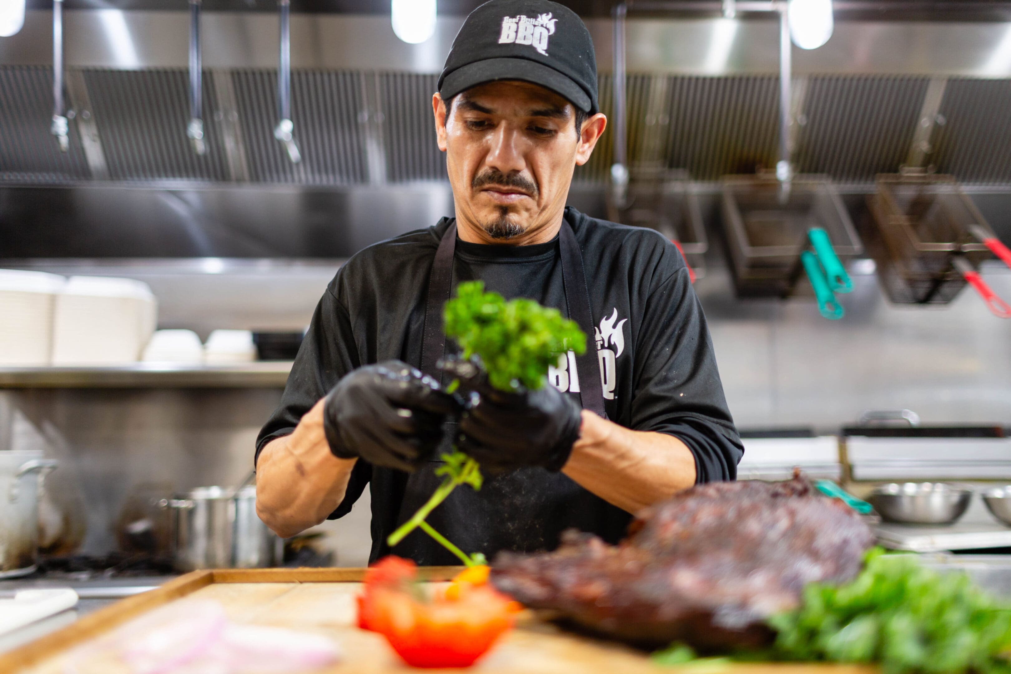 A man in black shirt holding green plant near meat.