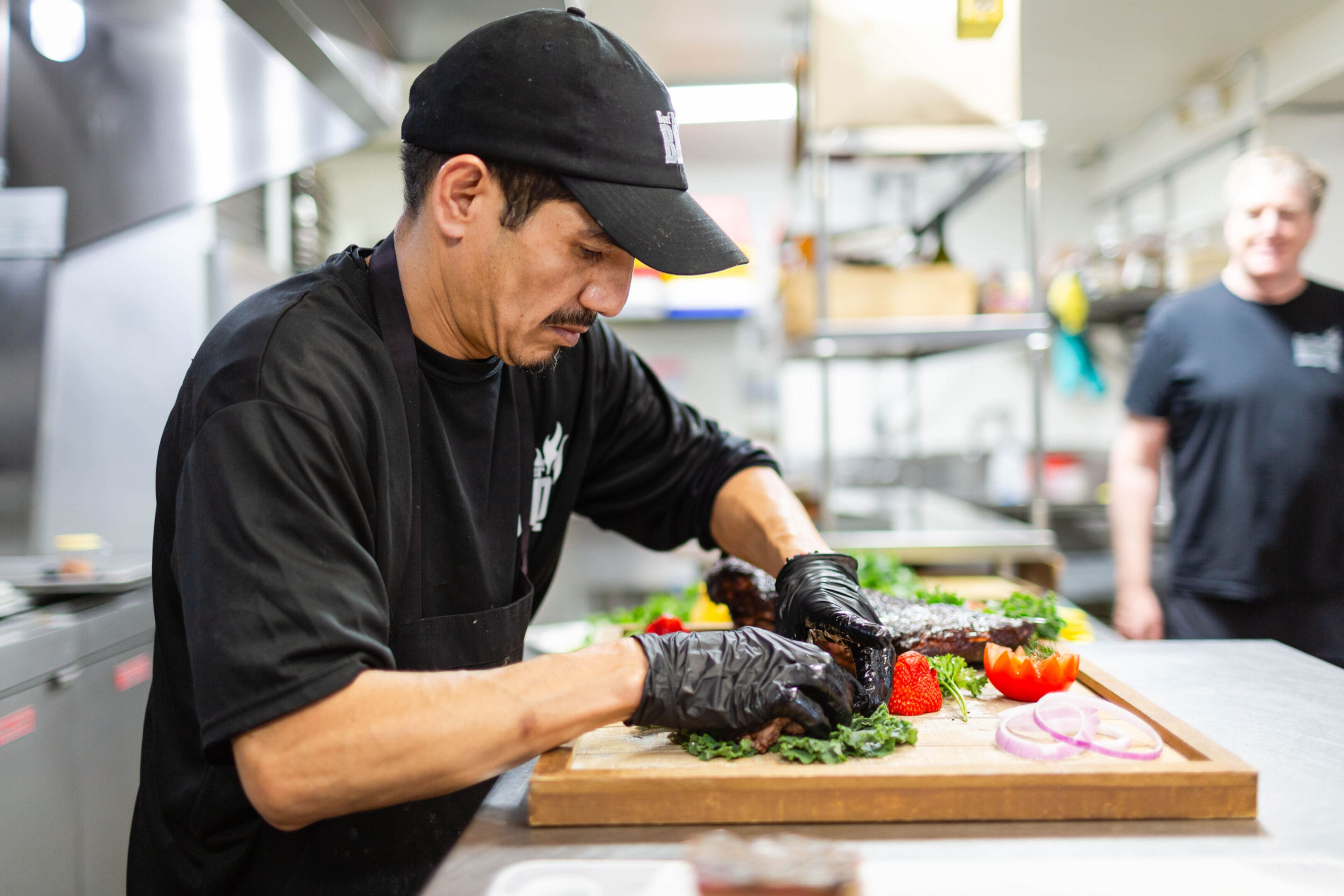 A man in black shirt cutting vegetables on wooden board.