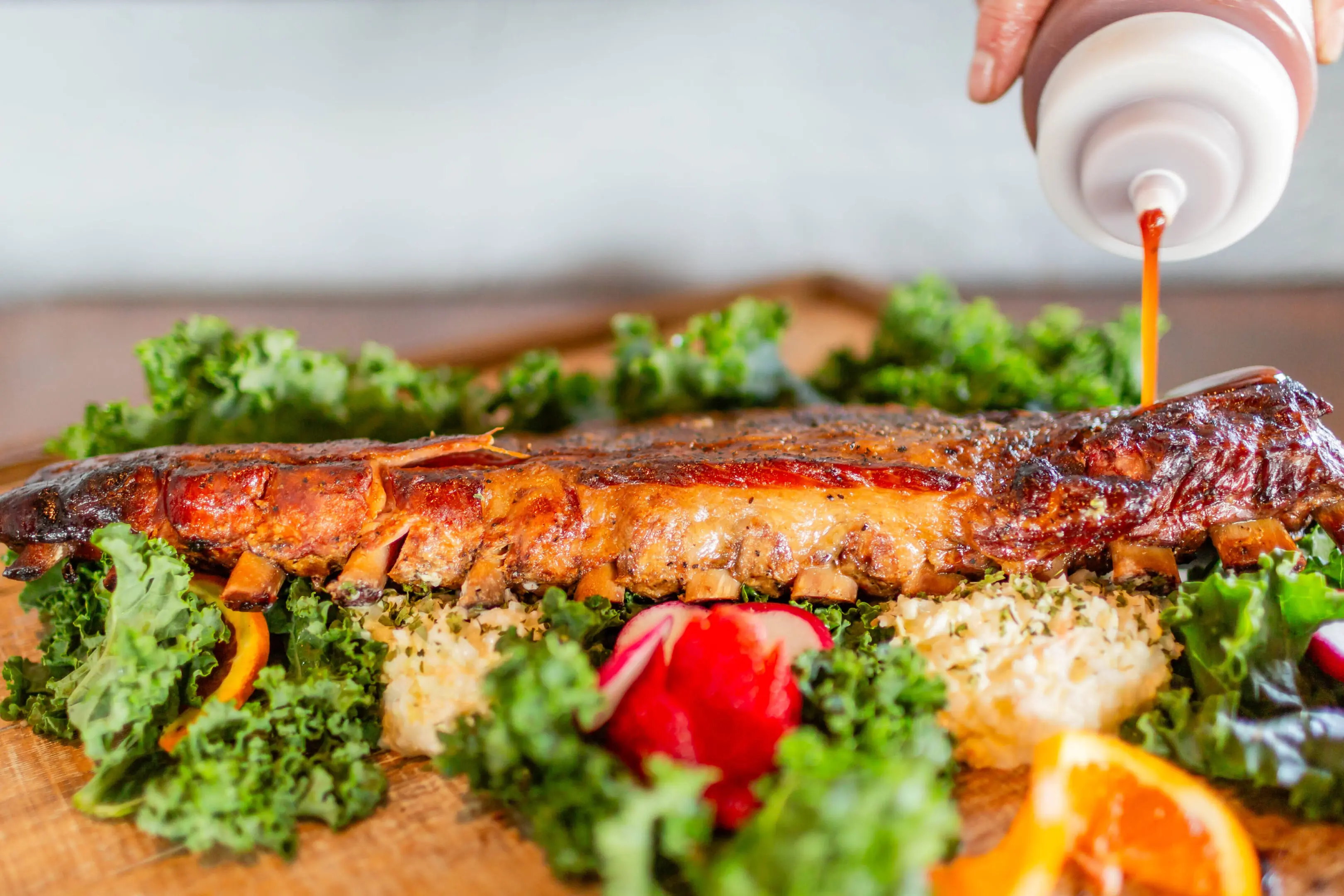 A person is holding a bottle of sauce over the food.