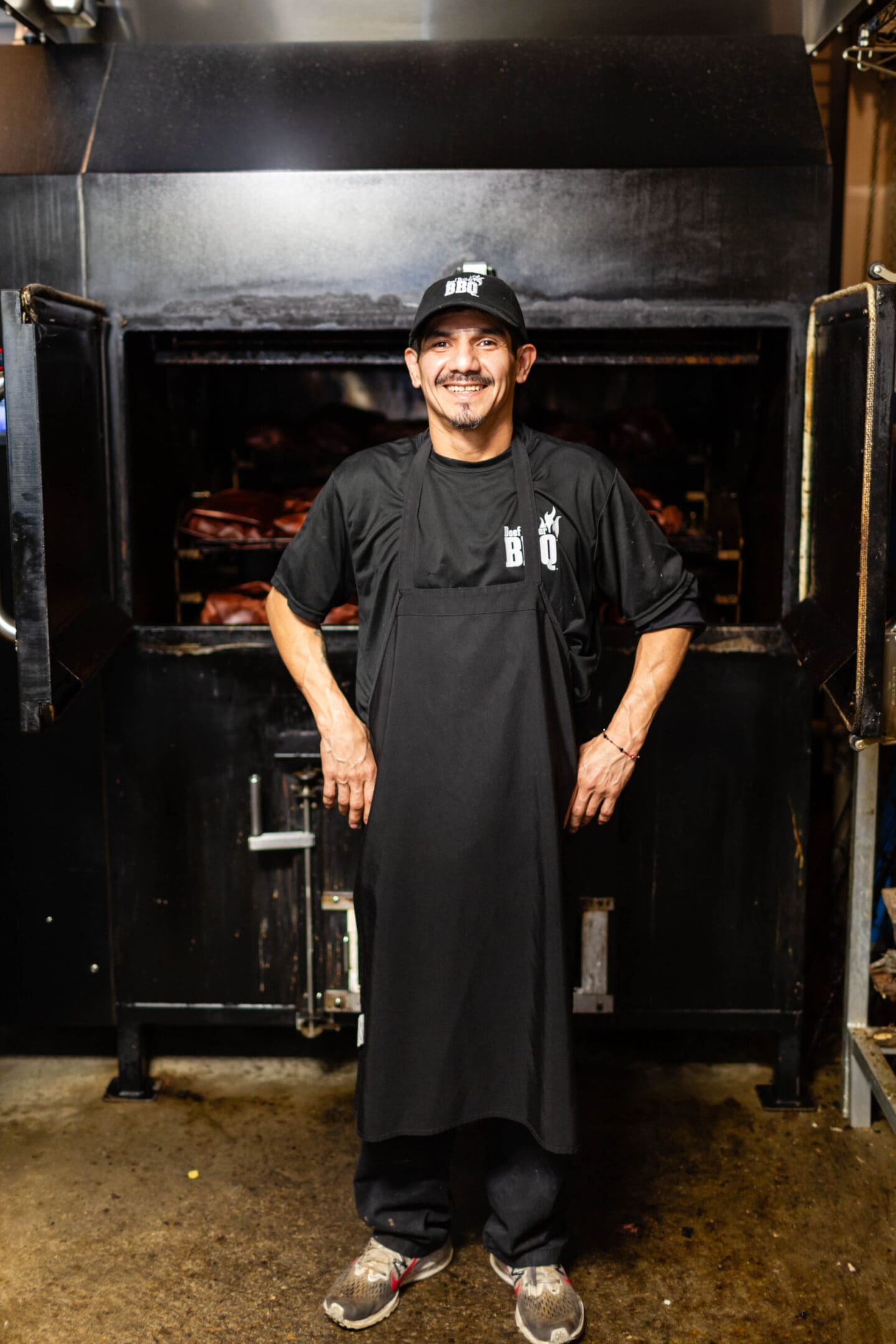 A man in an apron standing next to a large oven.